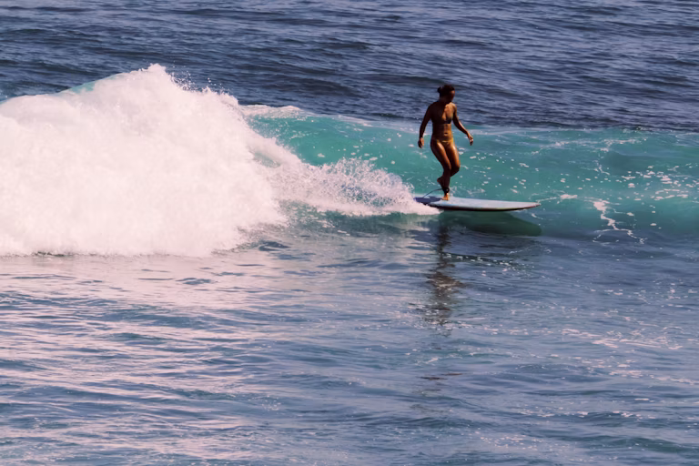 Persona surfeando con una tabla larga en una ola de Uluwatu, Bali